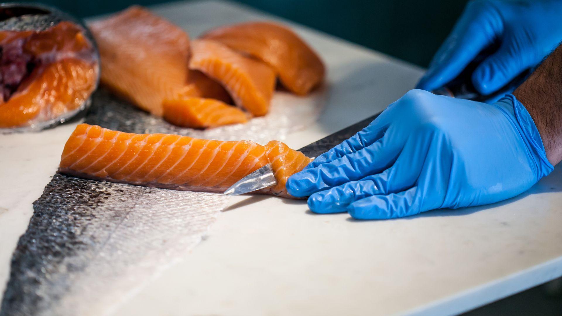 Trabajador experto cortando el salmón ahumado fresco a trozos