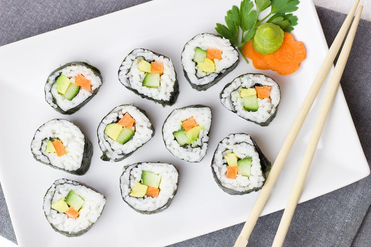 Plato de sushi con decoración con hojas verdes y salsas para mojar el sushi junto con palillos para mojar el sushi para dar un mejor sabor
