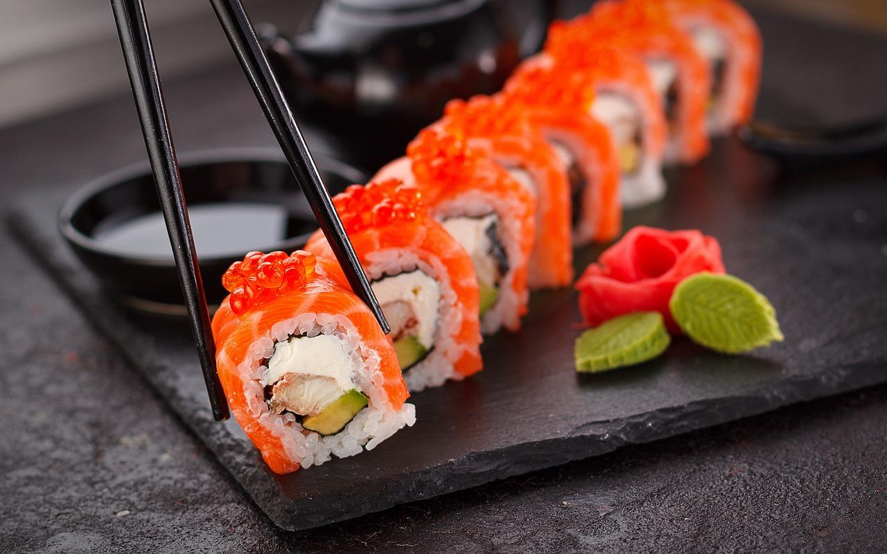 Sushi puesto en una Tabla de piedra con hojas para dar decoración al plato mientras una persona está cogiendo con unos palillos un trozo de sushi