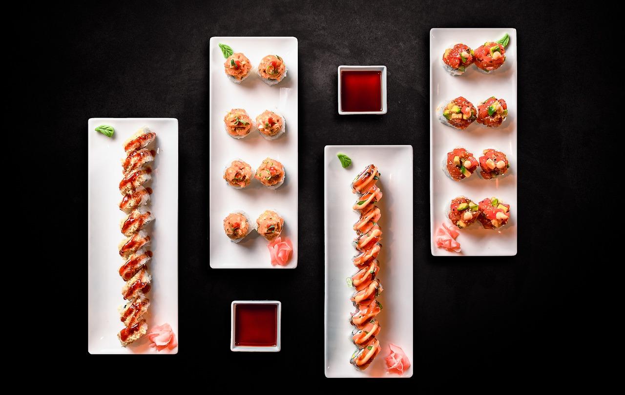 Diferentes sushis que se encuentran en diferentes platos con las salsas de color rojo que hay para mojarlo con el sushi